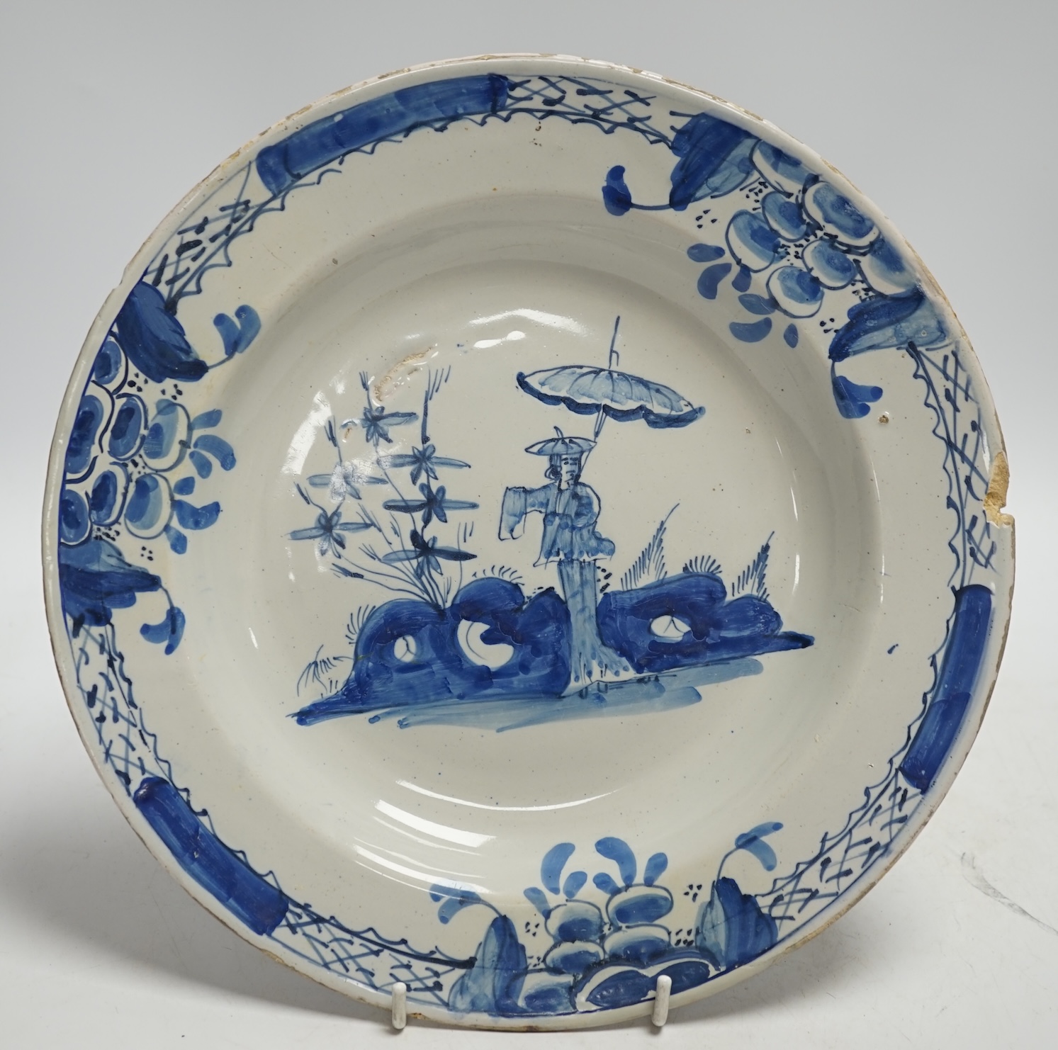 An 18th century Delft dish, decorated with a Chinese scene of a figure with a parasol, diameter 28cm. Condition - damaged to rim